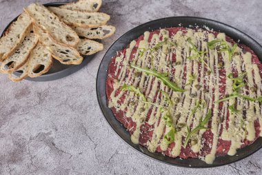 Carpaccio bifteği, parmesanlı soğuk aperatif, kapari ve roka, siyah tabakta seçici odaklanma.