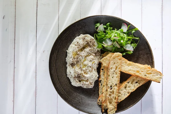 İtalyan peynirli stracciatella -bufalo mozzarella- taze roka ve kızarmış ekmekle servis edilen siyah tabakta. Şefin sunumu.