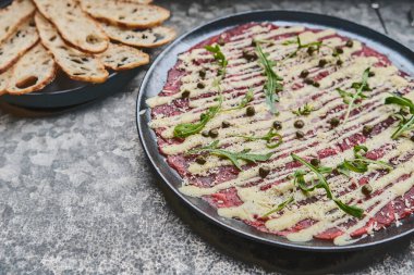 Carpaccio bifteği, parmesanlı soğuk aperatif, kapari ve roka, siyah tabakta seçici odaklanma.