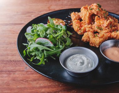 Kızarmış tavuk, gurme roka ve turp salatası, yanında da Peru biber sosu, siyah bir tabakta servis ediliyor..