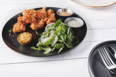 Kızarmış tavuk, gurme roka ve turp salatası, yanında da Peru biber sosu, siyah bir tabakta servis ediliyor..