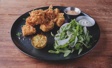 Kızarmış tavuk, gurme roka ve turp salatası, yanında da Peru biber sosu, siyah bir tabakta servis ediliyor..