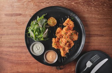 Kızarmış tavuk, gurme roka ve turp salatası, yanında da Peru biber sosu, siyah bir tabakta servis ediliyor..