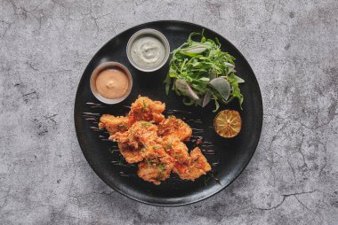 Kızarmış tavuk, gurme roka ve turp salatası, yanında da Peru biber sosu, siyah bir tabakta servis ediliyor..