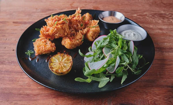 Kızarmış tavuk, gurme roka ve turp salatası, yanında da Peru biber sosu, siyah bir tabakta servis ediliyor..