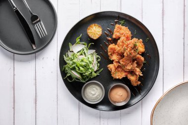 Kızarmış tavuk, gurme roka ve turp salatası, yanında da Peru biber sosu, siyah bir tabakta servis ediliyor..