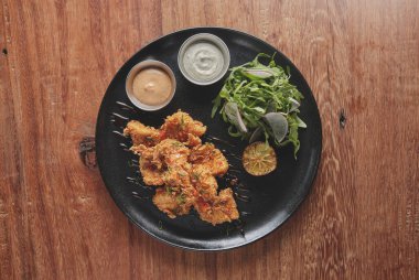 Kızarmış tavuk, gurme roka ve turp salatası, yanında da Peru biber sosu, siyah bir tabakta servis ediliyor..