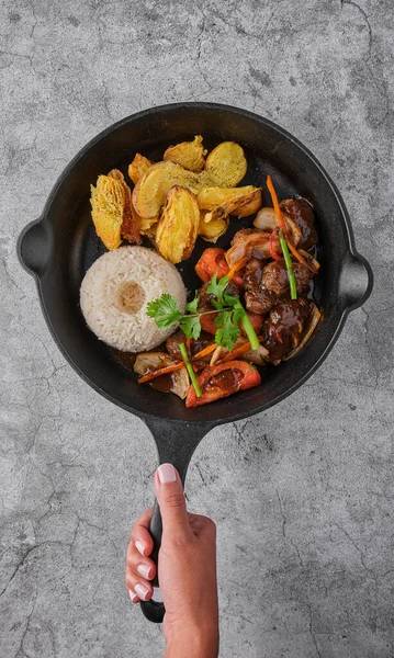 Peruvian d food - Lomo saltado - beef tenderloin with purple onion, yellow pepper, tomatoes served in a black pan with french fries and rice. Top view — Foto de Stock