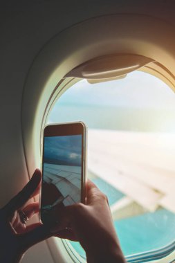 El, uçak penceresinden cep telefonunun fotoğrafını çekiyor..