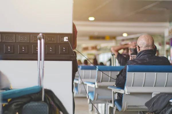 Senior man with smartphone charging devices in airport lounge with luggage hand-cart