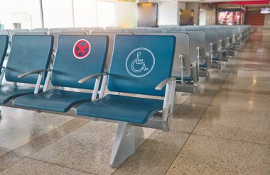 Havaalanının kalkış salonunda boş sandalyeler, arka planda bulanık bir uçak.