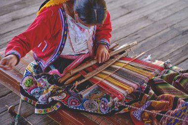 Indigenous woman showing traditional weaving technique and textile making in the Andes mountain range of South America in Peru.