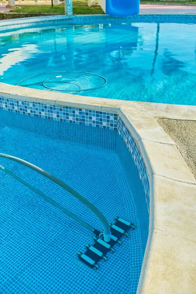 Worker cleaning outdoor pool with underwater vacuum early in the morning.