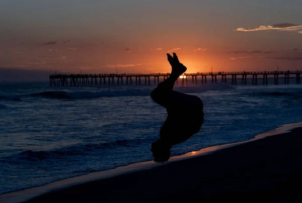 Back flip on the beach at sunset with a pier in the background