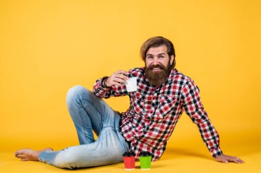 Mutlu, sakallı, sakalsız, şık saçlı, sıradan kıyafetler giyen, kahve içen, enerjik bir adam.