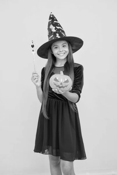 Menina feliz usar chapéu de bruxa segurando varinha mágica e abóbora jack o lanterna para criar encantamento no dia das bruxas, feitiçaria halloween — Fotografia de Stock
