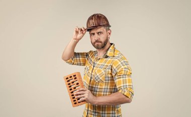 İnşaat kaskı ve inşaat alanında tuğladan yapılmış kareli gömlek giyen yakışıklı bir işçi.
