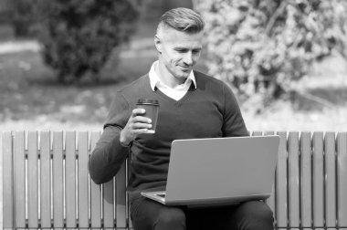 Güne güzel bir başlangıç. Günaydın. Olgun yakışıklı adam dışarıda bilgisayarda çalışıyor. Bakımlı adam bankta kahveyle oturuyor. Kendine güvenen iş adamı hatta. Sıradan iş modası. çevik iş