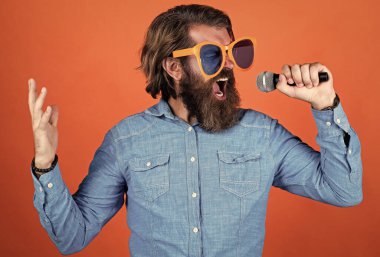 Duygularını ifade et. Mutlu sakallı adam komik parti gözlükleri takıyor. Olgun etkinlik yöneticisi mikrofonu tut. Biraz eğlen. Doğum günü partisi şarkıcısı. Tatili kutlayalım. Hipster şarkı söylüyor. müzik