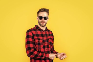 Kareli tişörtlü ve güneş gözlüklü genç yakışıklı adamın yüzünde kıllar, moda aksesuarları var.