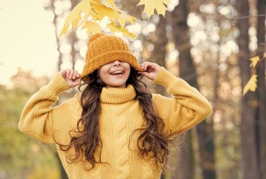 Sonbahar modası. Sonbahar eğlence zamanıdır. Çocuklar için sonbahar modası. Sonbahar tarzı çocuk. Örgü seni her havada ısıtır. Sarı örgü süveter ve şapkalı kız. Çocuk parkta doğanın tadını çıkarıyor.