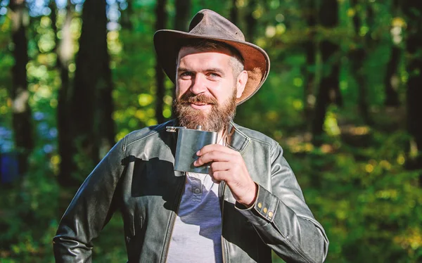 Estilo country. Hombre barbudo con sombrero de vaquero caminar en el parque al aire libre. hombre hipster relajarse en el bosque de otoño. Clima de primavera. camping y senderismo. macho maduro con aspecto brutal beber alcohol de matraz metálico —  Fotos de Stock