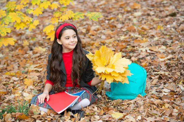 Boldog gyermek egyenruhában tartsa őszi juhar levelek iskolatáska és notebook szabadban, iskola — Stock Fotó
