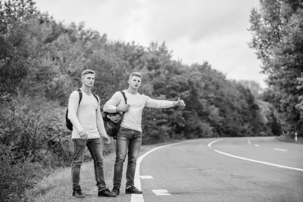 Typ av äventyr. På vägen. Njuter av sommarvandringen. Letar efter transport. Tvillingar som går längs vägen. Stanna bilen med tummen upp gest. liftar och stannar bil med tummen upp gest — Stockfoto