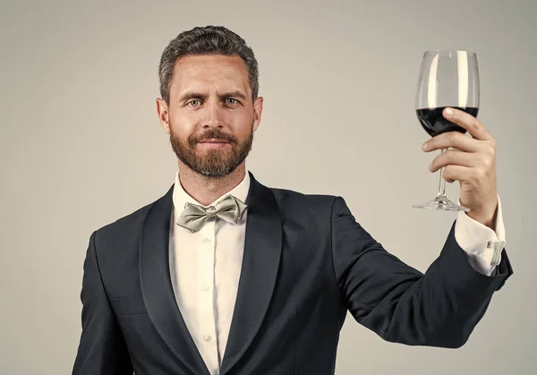 handsome tuxedo man in bow tie cheers with glass of red wine, anniversary
