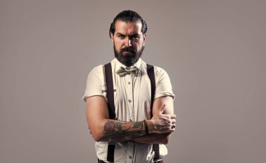 Olgun erkek hippi pantolon askısı takar ve papyon takar. Saçları, sakalı, modası ve kuaförü çok bakımlıdır.