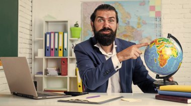 Sakallı ve bıyıklı bir adam üniversitede ya da okulda iş adamı ya da öğretmen gibi görünüyor.