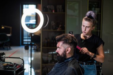 Size nasıl yardımcı olabilirim? Erkek berber bakımı. Kuaför salonundaki sakallı adam. Güzellik ve moda. Saç ve sakal şekillendirme. Profesyonel berber ustası olan vahşi adam elektrikli tıraş makinesi kullanıyor.