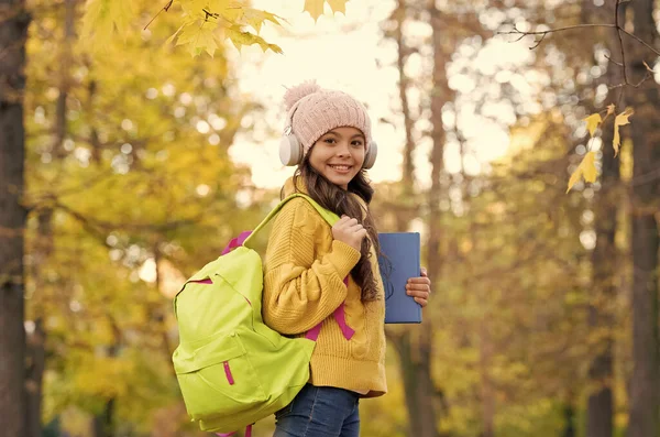 kid listen music in autumn park. fall is a time for study. back to school. concept of online education. child carry books for study. girl in earphones with school bag