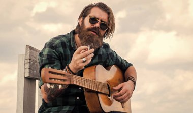 Müzik aleti olan erkek gitarist. Country müzik konsepti. Sakallı adam akustik gitar çalar. Sıradan bir adam insani duygularını ifade eder. Uzun saçlı hippi ve bıyıklı gitarist. Ritmi oynat