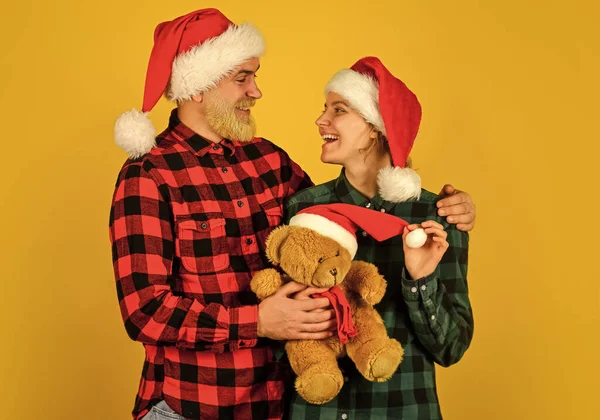 We houden van kerst. Houden van een paar gele achtergrond. Kersttijd. Paar verliefd op teddybeer zacht speelgoed genieten van kerstvakantie. Familie santa hoeden. Entertainment ideeën voor volwassenen. Gezinsvakantie — Stockfoto