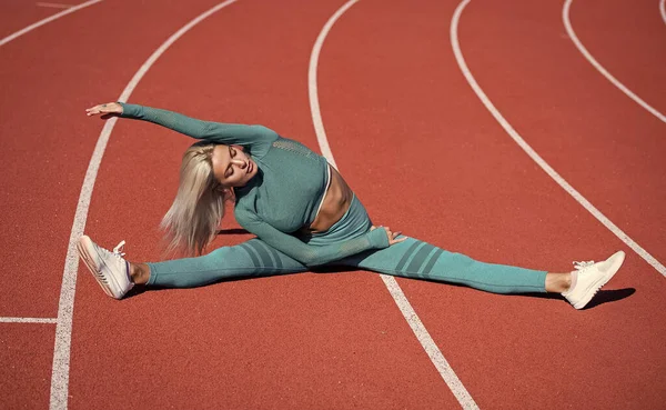 Mujer con cuerpo de fitness sexy en ropa deportiva que se extiende en el estadio, dividir — Foto de Stock