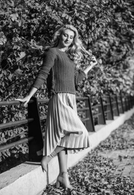 Sevimli gülümseyen kadın. Yapraklarla güneşli bir gün. Sonbahar moda sezonu. Etek ve süveter giyen kız. Pileli trend. Kadın güzeli. Kadınlık ve şefkat. Sonbahar kadını dışarıda. Parktaki kız