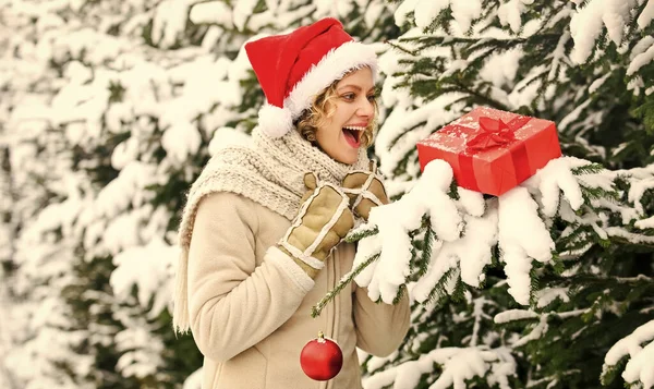 Por Dios, sé alegre. mujer feliz celebrar la caja regalo de Navidad. chica con la decoración del árbol de Navidad. Señora santa gorra roja en el árbol de piel. compras de invierno felicidad. clima brillante es el estado de ánimo prefecto. venta y descuento — Foto de Stock