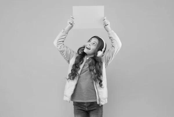 Sehen Sie sich das an. zurück zur Schule. Kind hält leeres Papier für Kopierraum. Online-Bildungsankündigung. Werbetechnik. Kindheitsentwicklung. glückliches Kind mit Kopfhörer Musik hören — Stockfoto