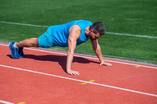 Atlético muscular homem fazendo push ups ao ar livre no estádio, poder — Fotografia de Stock