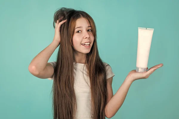 Χαρούμενο κορίτσι παιδί με μακριά ίσια μαλλιά κρατήστε conditioner σαμπουάν ή τζελ μπουκάλι, περιποίηση μαλλιών — Φωτογραφία Αρχείου