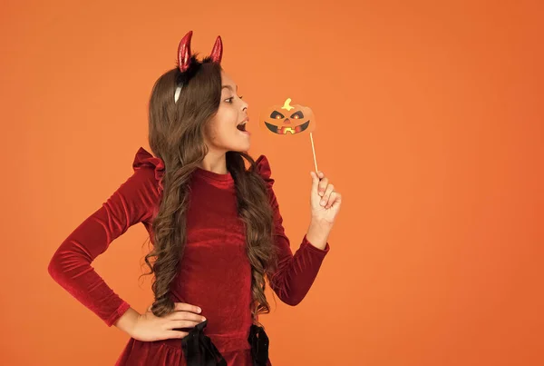 Grappig kind met lang haar dragen duivel hoorns houden partij accessoire pompoen voor herfst Halloween vakantie viering, gelukkig Halloween. kopieerruimte — Stockfoto