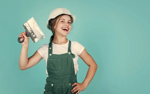 Woningrenovatie. Een jongen met gereedschap. gelukkig klein bouwmeisje met spatel. tiener meisje gebruik stoppelmes. bouwer in overall en helm met spatel. Jongen reparatie muur met spackling pasta. kopieerruimte — Stockfoto