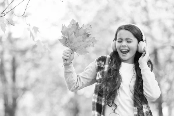 Trendig skönhet. barndoms lycka. skönhet och natur. Glad unge bär hörlurar. Tonårstjejen lyssnar på musik på väg till skolan. barnvandring i höstskogen. faller lönnlöv i parken. Internetutbildning. — Stockfoto