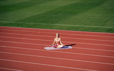 Formda bayan spor sonrası stadyumda meditasyon yapıyor, yoga yapıyor.