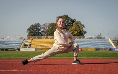 Koşucu yarış için hazırlan. Stadyum salonunda sprinter ısınıyor. Esneklik. Beden eğitimi dersinde çocuk eğitimi. Genç kız koşmadan önce geriniyor. Formda ve sağlıklı kalmak.