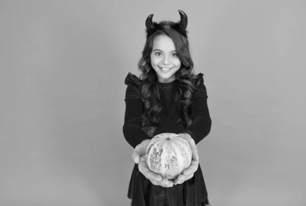 Feliz Dia das Bruxas. Criança sorridente com chifres de diabo. criança segure vegetal de abóbora. comida tradicional de férias e colheita de outono. felicidade infantil. menina adolescente pronto para celebrar festa traje — Fotografia de Stock