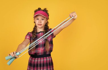 Spor aletleri tutan mutlu bir kız. Çocuk tenis raketini tutuyor. Çocuk ftness şapkası takıyor. Çocukluk aktivitesi. Sağlıklı bir yaşam tarzı. Enerjik ol.