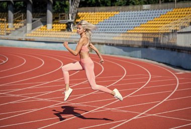 Stadyum koşu pistinde koşan atletik bayan. Bayan sporcu sprint sporu için hazır. Antrenör ya da koç eğitimi. Maraton. Enerjik ve sportif. Spor giyim sektöründe seksi bir kadın.