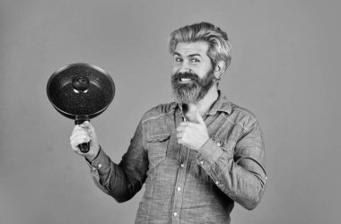 Sakallı adam, yemek tepsisini tut. Mutfakta yemek pişir. Kocası mutfakta. Yemek pişirme konsepti. Tavayı tut. En iyi kalite Sakallı aşçı portresi ve mutfak aletleri